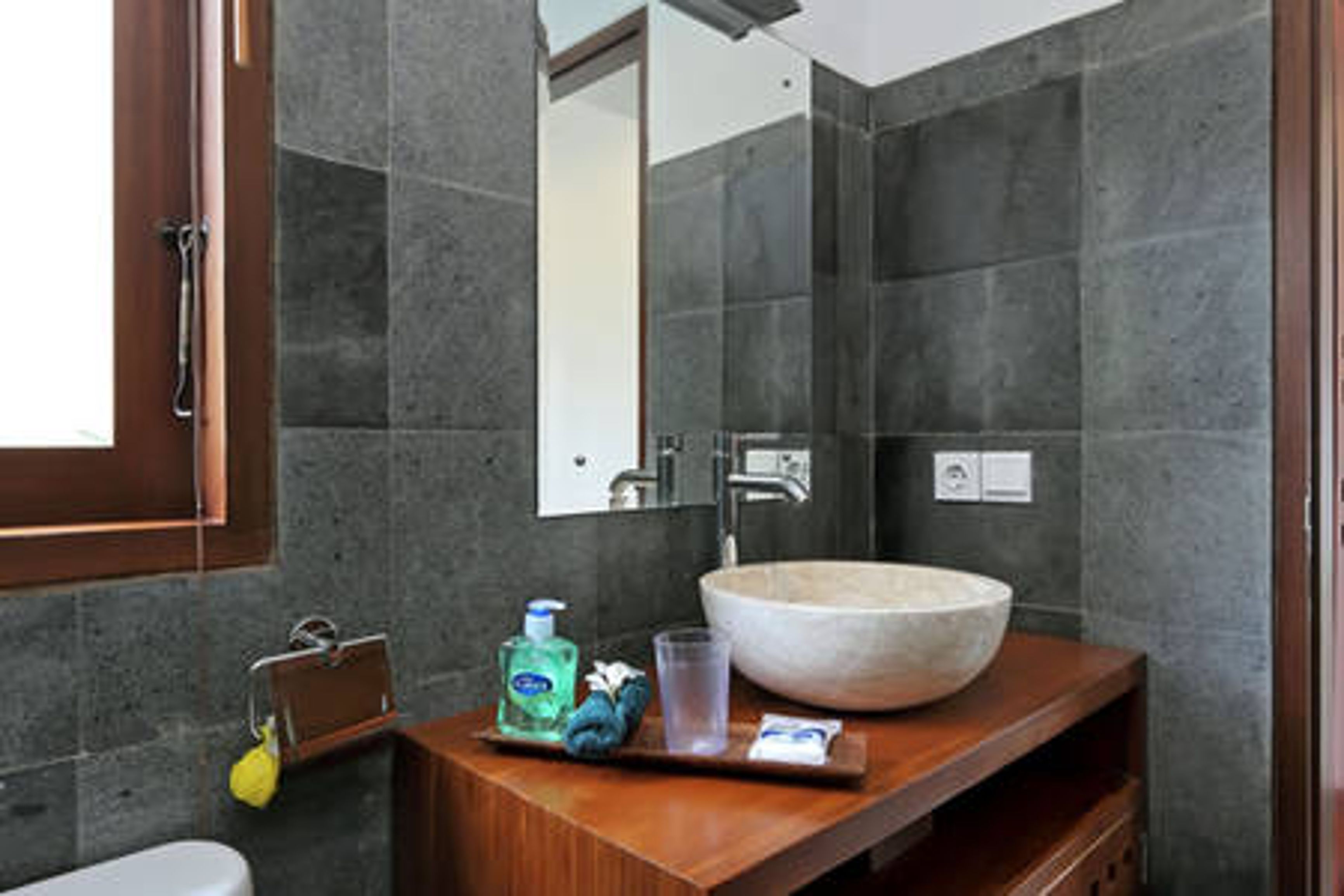 A modern bathroom with a large stone sink, a wooden vanity, a mirror, and a towel rack.