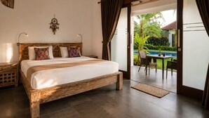 A bedroom with a wooden bed, a nightstand, a dreamcatcher, and a view of a pool and outdoor seating area. - Bali Mynah Villas Balangan (Jimbaran)