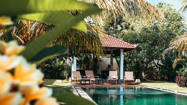 A pool area with lounge chairs and a gazebo, surrounded by tropical plants. - Bali Mynah Villas Balangan (Jimbaran)