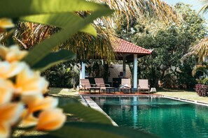 A pool area with lounge chairs and a gazebo, surrounded by tropical plants.