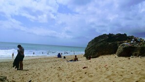 A sandy beach with a large rock formation, waves, and people in the water. - Bali Mynah Villas Balangan (Jimbaran)