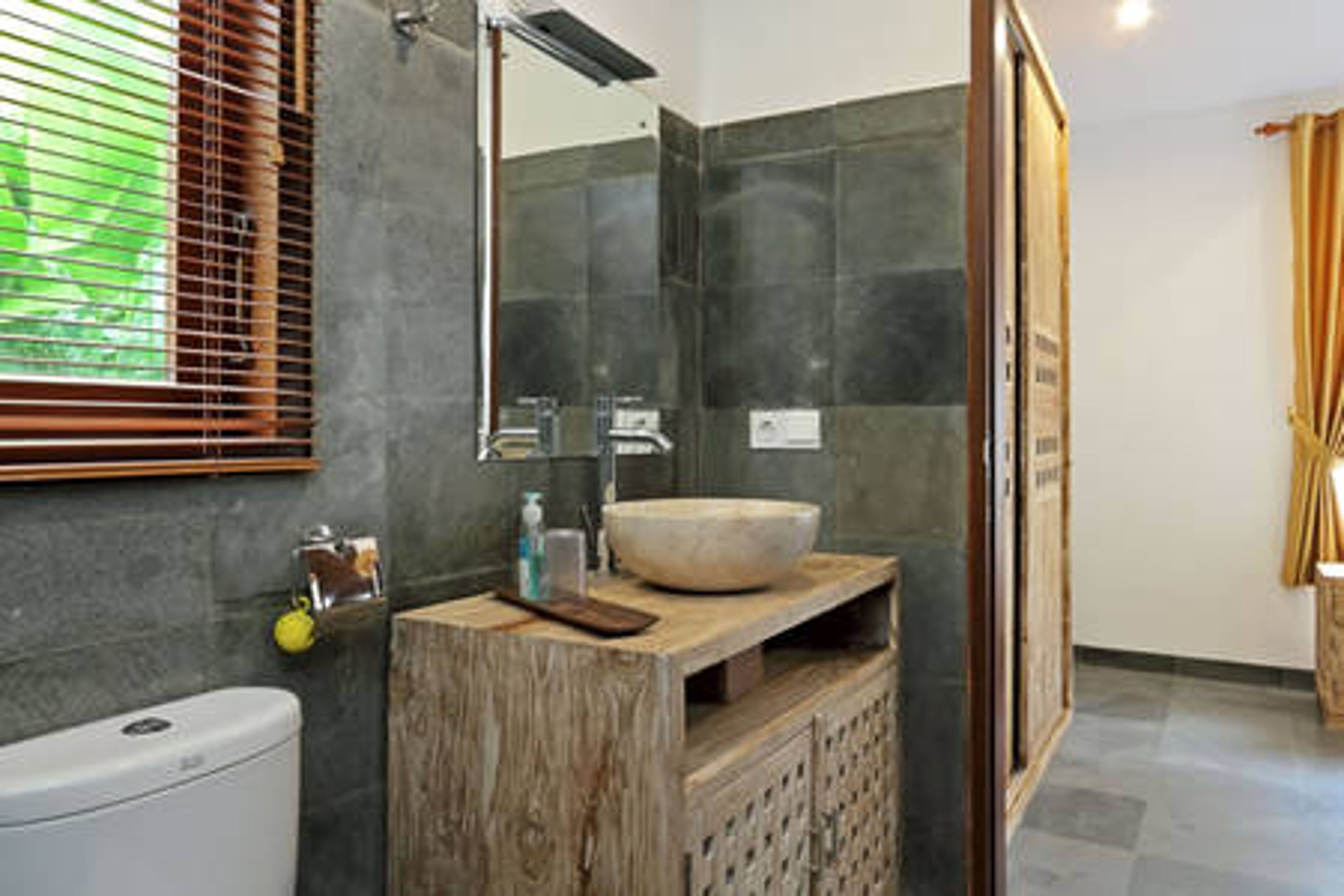 A bathroom with a wooden vanity, a large mirror, a round sink, and a shower area.