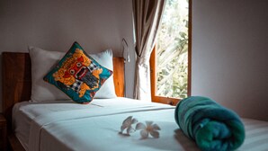 A neatly made bed with a colorful pillow, a rolled towel, and a white flower on the bed. - Bali Mynah Villas Balangan (Jimbaran)