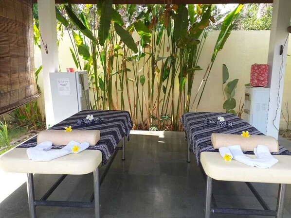 Two massage tables with towels and flowers, surrounded by plants and a bamboo backdrop.