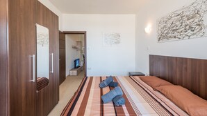 A modern bedroom with a large bed, wooden wardrobe, and artwork on the walls. - GetawaysMalta - Seashells 2-bedroom Apartment in Bugibba (San Pawl il-Baħar)