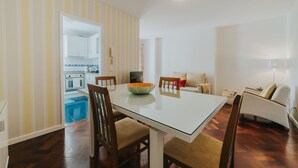 A dining area with a glass table, wooden chairs, and a kitchen in the background. - Casa da Calçada - 2nd Floor (Funchal)