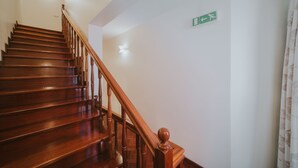 A wooden staircase with a handrail and a green emergency exit sign on the wall. - Casa da Calçada - 2nd Floor (Funchal)