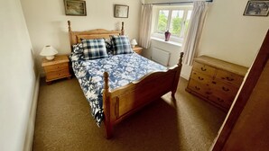Een slaapkamer met een houten bed, nachtkastje, dressoir en een raam met gordijnen.
