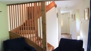 Een trap met houten leuningen, twee donkerblauwe fauteuils en een hal met ingelijste foto's.