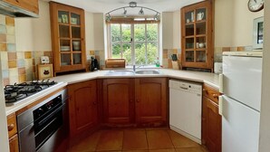 Een keuken met houten kastjes, een gasfornuis, een vaatwasser en een raam met uitzicht op groen.