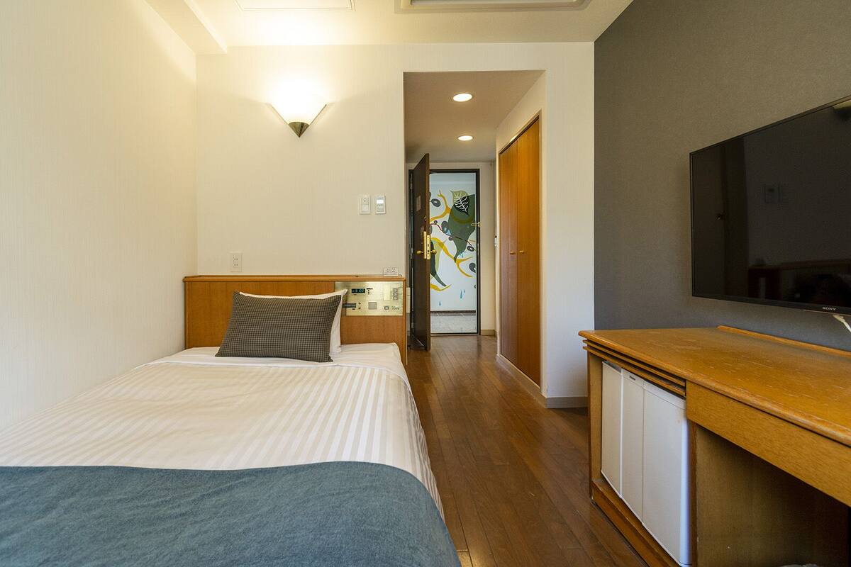 Habitación de hotel con cama, mesita de noche, televisor y panel de control.