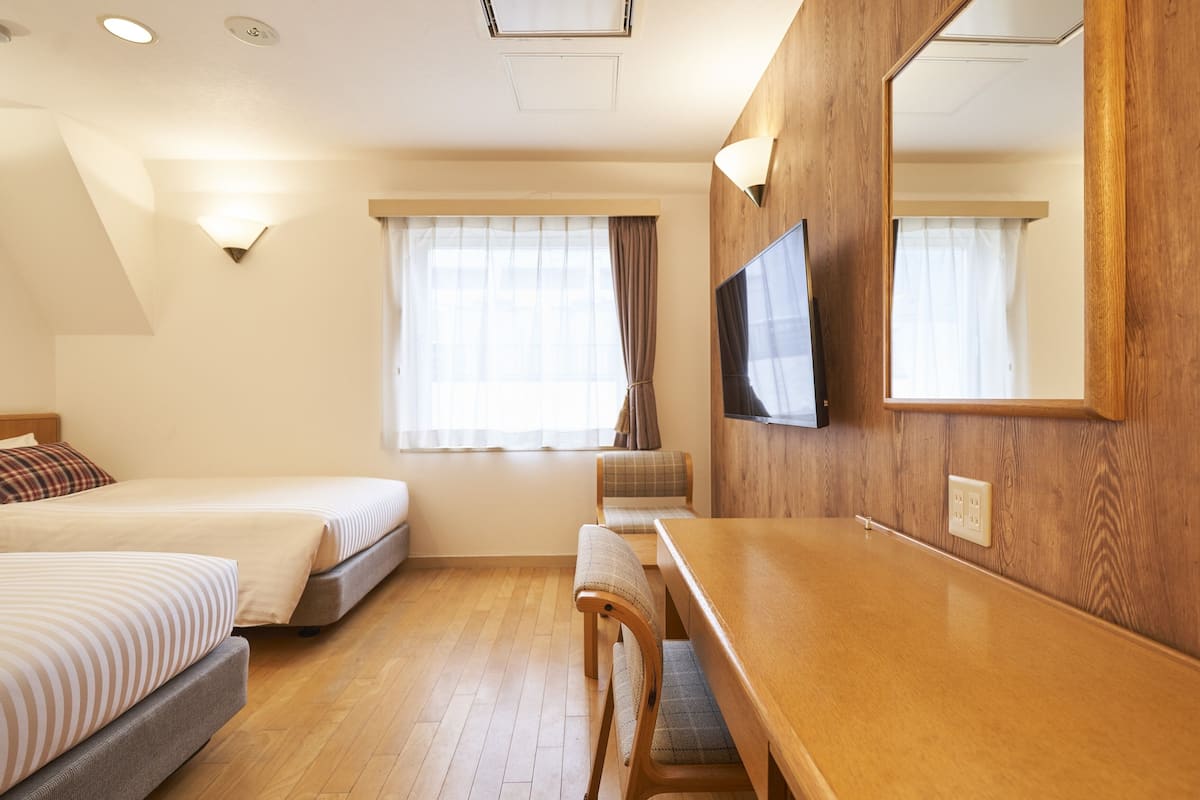 Habitación de hotel con cama, escritorio, silla, televisión y ventana con cortinas.
