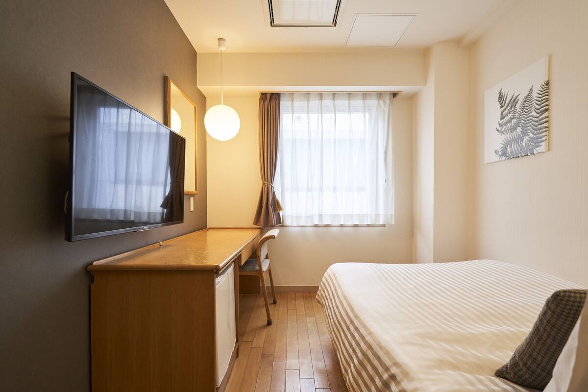 Habitación de hotel con cama, escritorio, televisión, ventana con cortinas y una obra de arte en la pared.
