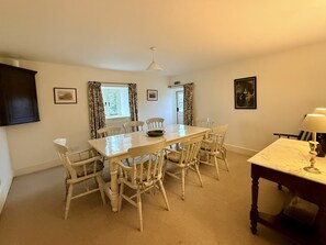 A dining room with a large table and six chairs, a small table with a lamp, and two windows with curtains. - Ty Newydd, Bodnant Estate, Colwyn Bay, Conwy, Wales (Colwyn Bay)