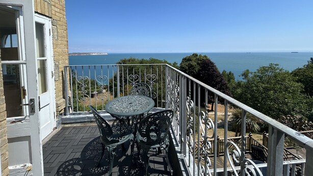 Un balcon avec une table et des chaises, offrant une vue sur la côte.