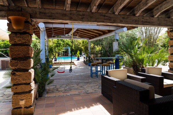 A covered outdoor area with wicker furniture, a pool, and stone flooring.