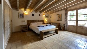 Een slaapkamer met een houten plafond, een groot bed, nachtkastjes en een raam met uitzicht op groen.