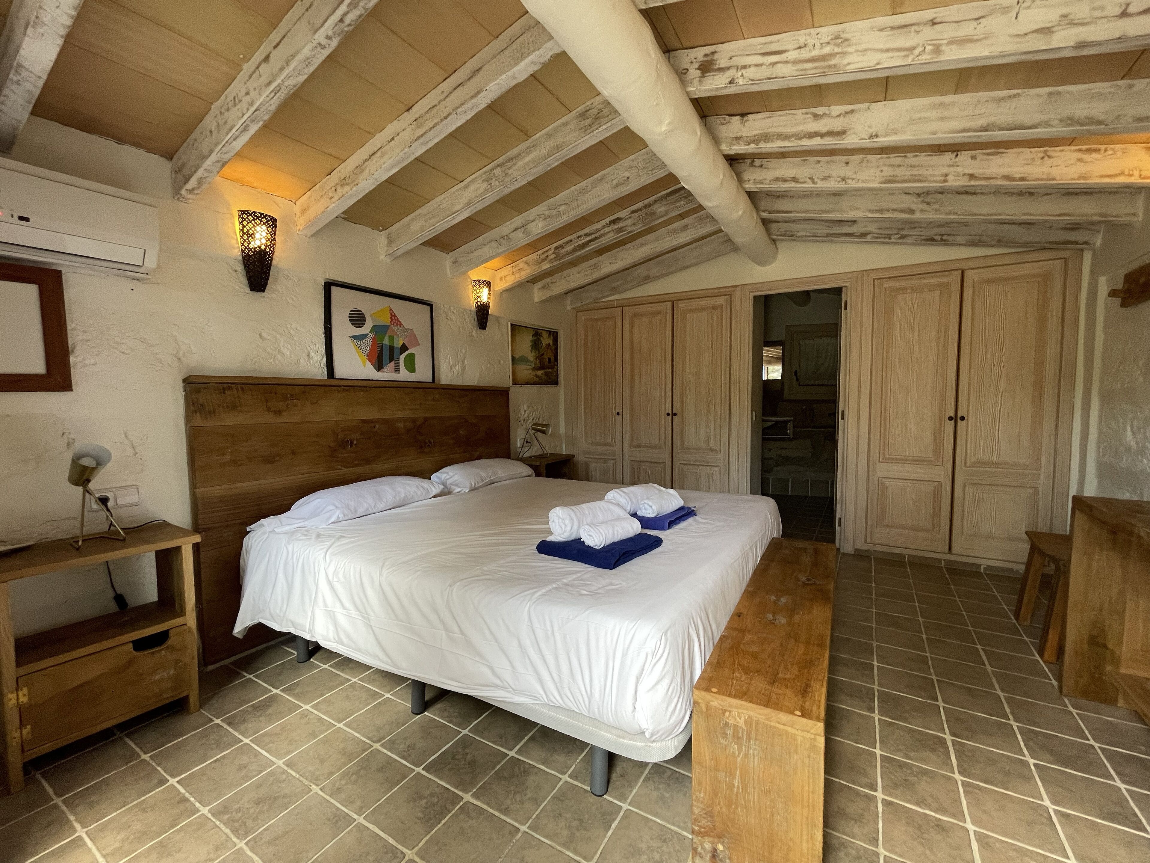 Une chambre à coucher avec une tête de lit en bois, un grand lit, un banc en bois et un sol carrelé.