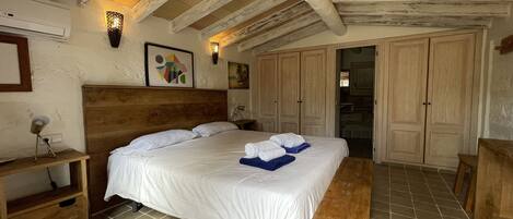 Une chambre à coucher avec une tête de lit en bois, un grand lit, un banc en bois et un sol carrelé.