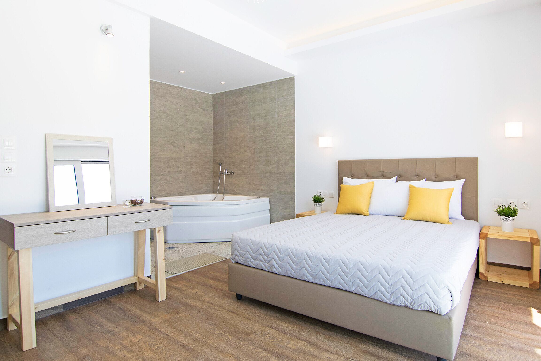 Una camera da letto moderna con un letto grande, una scrivania in legno, una vasca da bagno integrata e un piccolo comodino con una pianta.