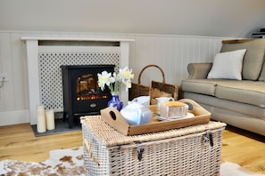 A cozy living room with a fireplace, a wicker basket with a cake, and a vase with flowers.