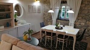 A cozy dining area with a stone wall, a white table, and four chairs. There is a round mirror above the table and a shelf with decorative items. - Cute vacation house surrounded by green area (Buzet)