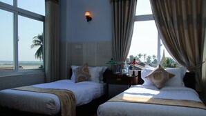 A hotel room with two beds, a nightstand, a lamp, and a view of the beach and temple. - King Hotel (Katha)