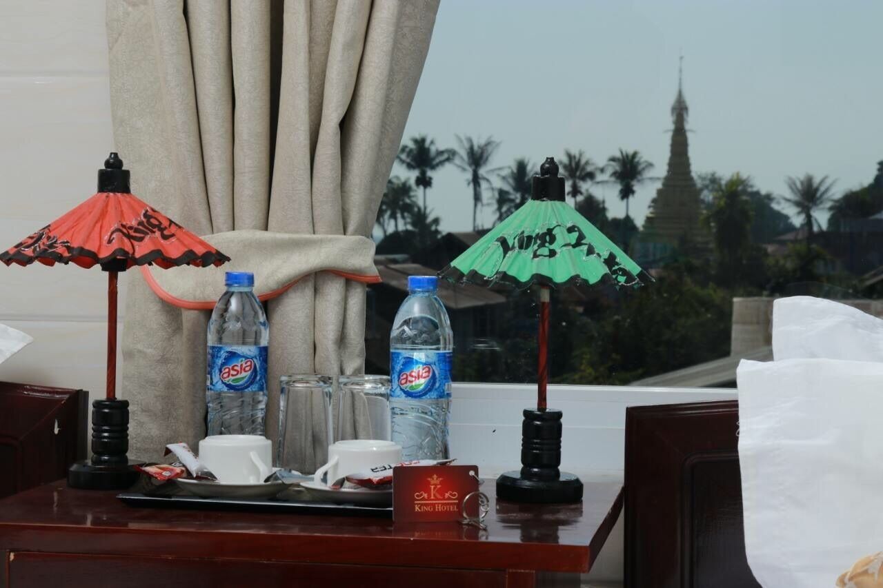 A hotel room with a table set with two bottles of Asia water, a cup, and a tray. There are two umbrellas, one red and one green, and a sign that reads "King Hotel".
