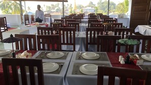 A restaurant with tables set for dining, chairs, and umbrellas. - King Hotel (Katha)