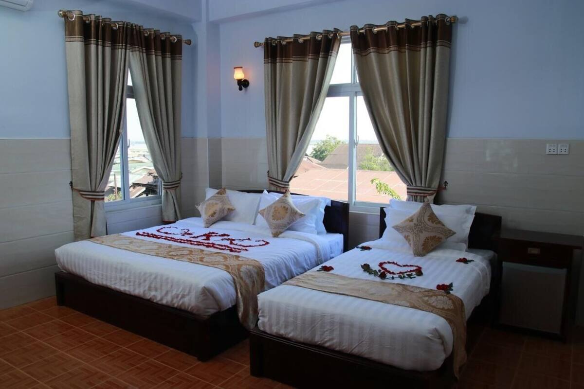 Une chambre d’hôtel avec deux lits, chacun agrémenté de draps blancs et d’oreillers décoratifs. On y trouve une petite table de chevet et une lampe fixée au mur.