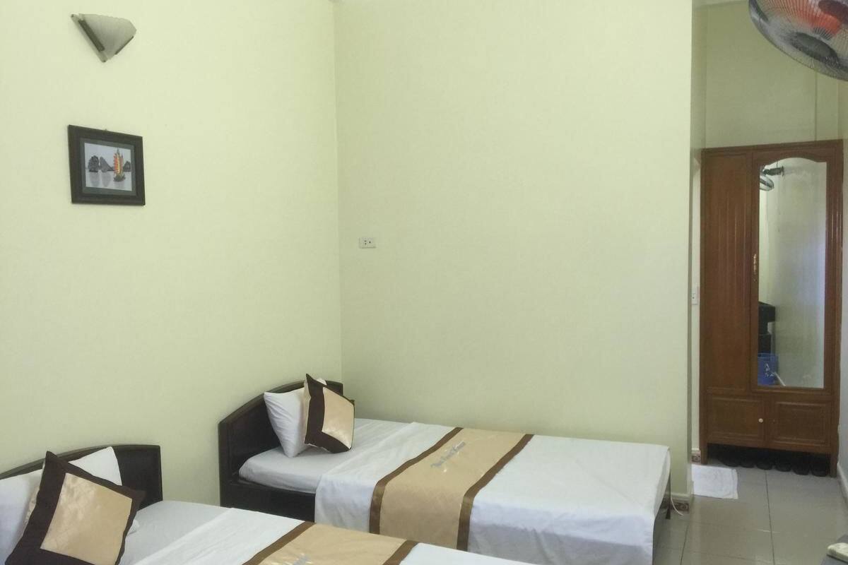 Habitación de hotel con dos camas individuales, una mesita, una silla, una lámpara en la pared y una puerta con espejo.