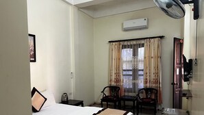 A hotel room with a bed, a desk, two chairs, a small refrigerator, an air conditioner, and a door with a lock. - Thu Guest House (Ninh Binh)