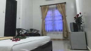 A hotel room with a bed, a desk, a chair, a window with curtains, an air conditioner, and a small refrigerator. - Thu Guest House (Ninh Binh)