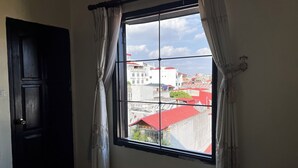 A room with a large window, a black door, and a view of buildings with red roofs. - Thu Guest House (Ninh Binh)