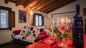 Una habitación acogedora con techo de madera, un sofá estampado de lunares, dos copas de vino y una botella de vino Eluan sobre una mesa roja.