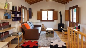 Una sala de estar acogedora con un sofá marrón, techo de madera, chimenea y estantería.