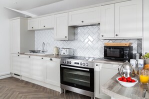 A modern kitchen with white cabinetry, a hob, oven, microwave, and a breakfast setup with fruits and juice.