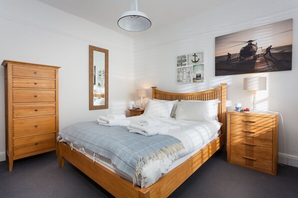 A bedroom with a wooden bed, a nightstand, a dresser, a mirror, and a wall with nautical-themed decor.
