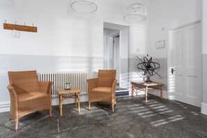 A room with two wicker chairs, a small wooden table, a radiator, and a white door.