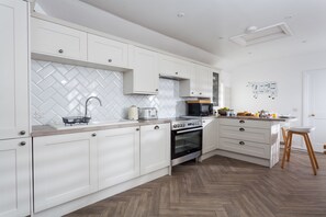 A modern kitchen with white cabinetry, a herringbone tile backsplash, and a wooden herringbone floor.