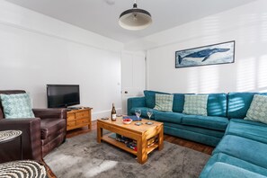 A living room with a teal sofa, a brown leather chair, a wooden coffee table, and a television on a stand.