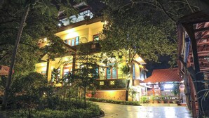 A multi-story building with balconies, surrounded by lush greenery and illuminated by warm lighting. - Hoang Giang Homestay (Ninh Binh)