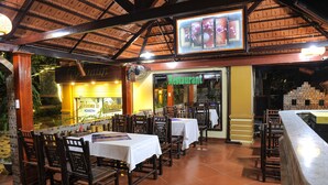 An outdoor restaurant with wooden tables and chairs, a thatched roof, and a sign reading "Restaurant". - Hoang Giang Homestay (Ninh Binh)