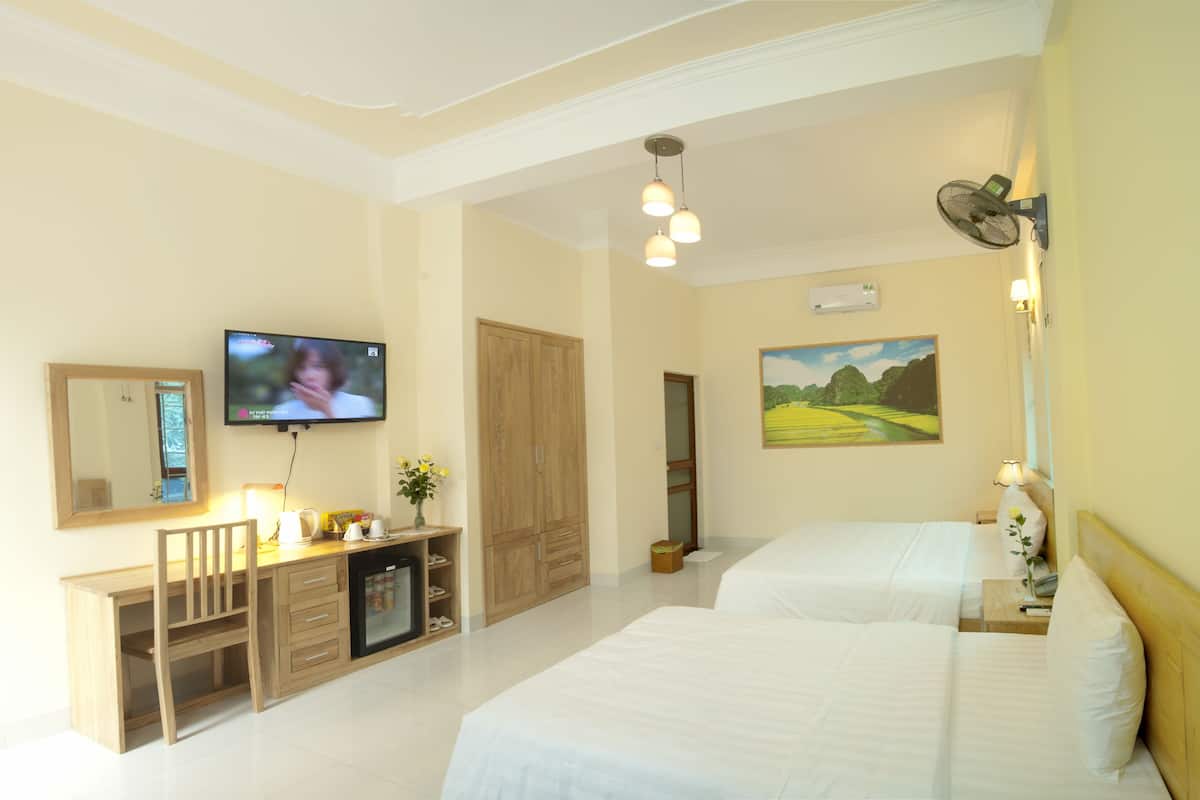 Ein Hotelzimmer mit Fernseher, Schreibtisch mit Stuhl, Kleiderschrank, zwei Betten und einem Bild an der Wand.