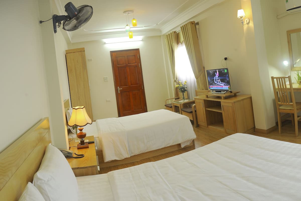 Ein Hotelzimmer mit zwei Betten, einem Schreibtisch mit Computer, einem Sessel, einer Lampe und einem Spiegel.