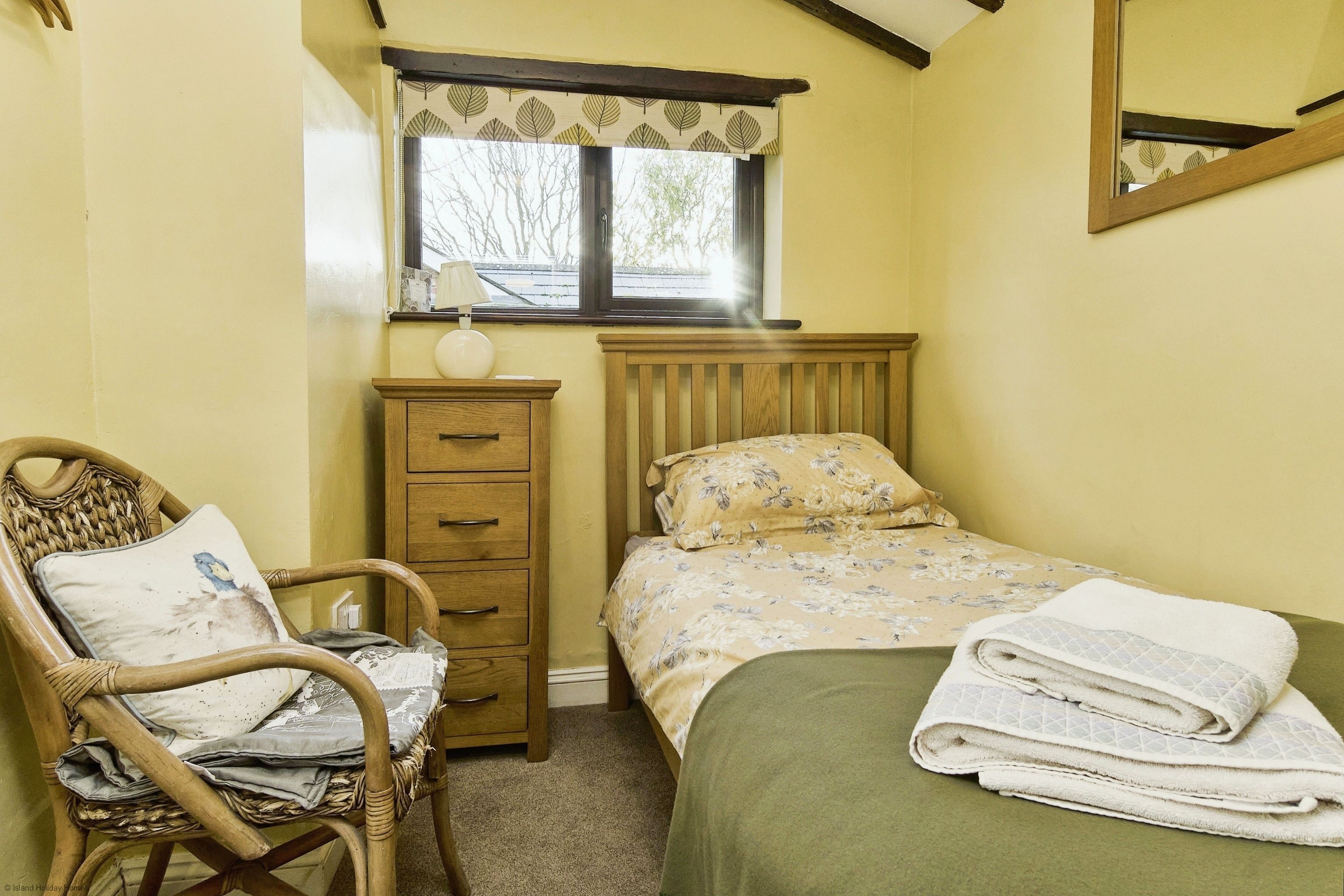 Un dormitorio con cama, una silla, un tocador y una ventana con vistas a árboles.