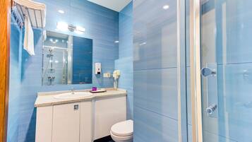 Ein modernes Badezimmer mit blauen Fliesen, einem Waschbecken mit Spiegel darüber, einer Toilette und einer Duschkabine aus Glas.