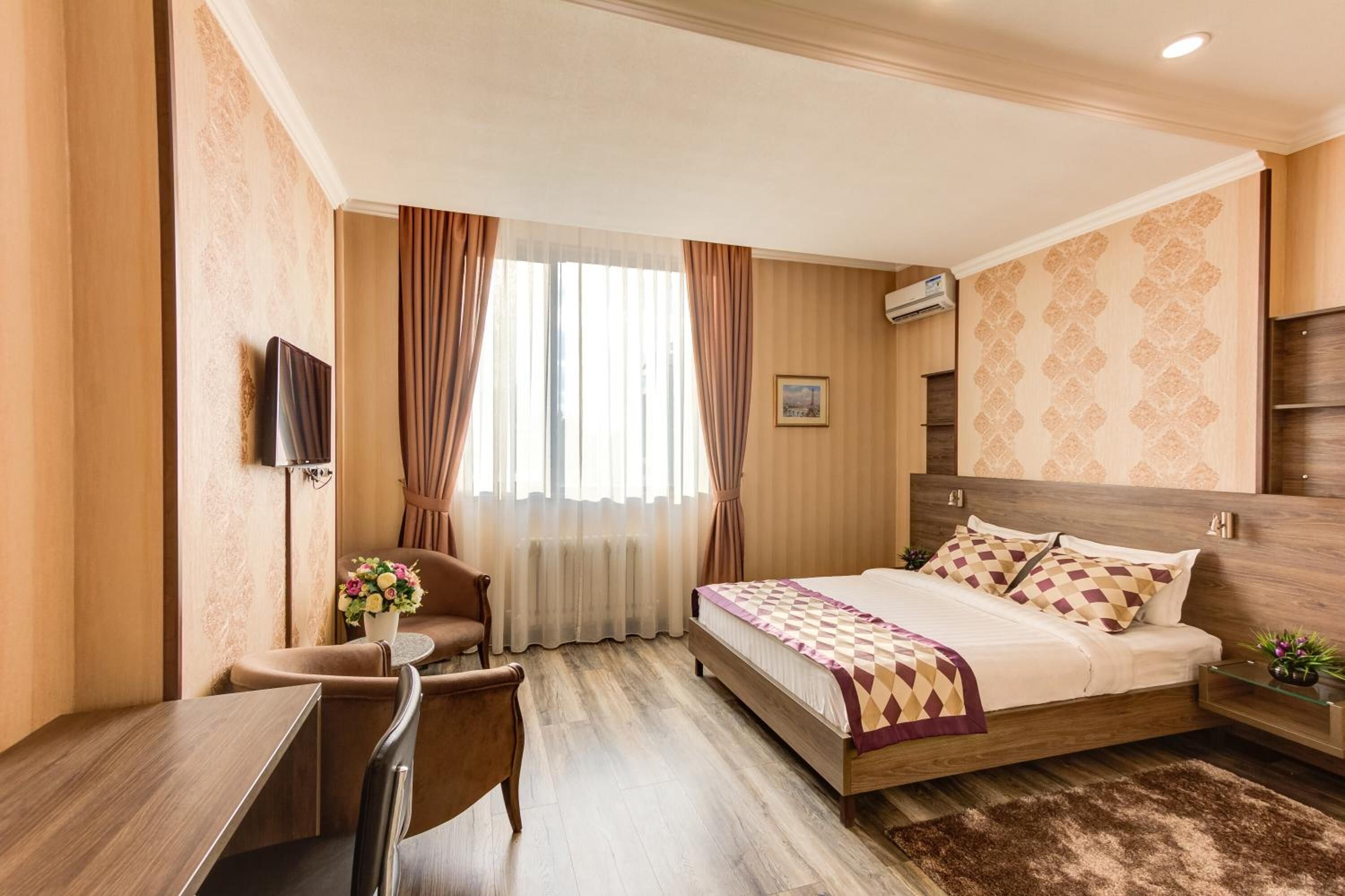 Ένα δωμάτιο ξενοδοχείου με ένα ξύλινο κρεβάτι, ένα γραφείο, μια καρέκλα και μια τηλεόραση.