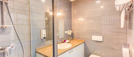 Un baño moderno con cabina de ducha de vidrio, lavabo con tocador, inodoro y ganchos para toallas.