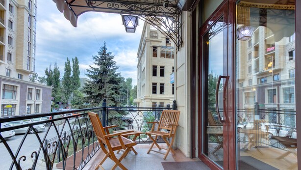 A balcony with two wooden chairs and a table, overlooking a street with parked cars and trees. - Bishkek Centrum Hotel (Bishkek)